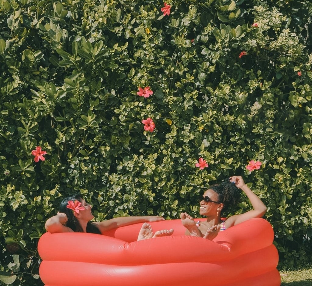Two people lounging in a red heart-shaped inflatable pool