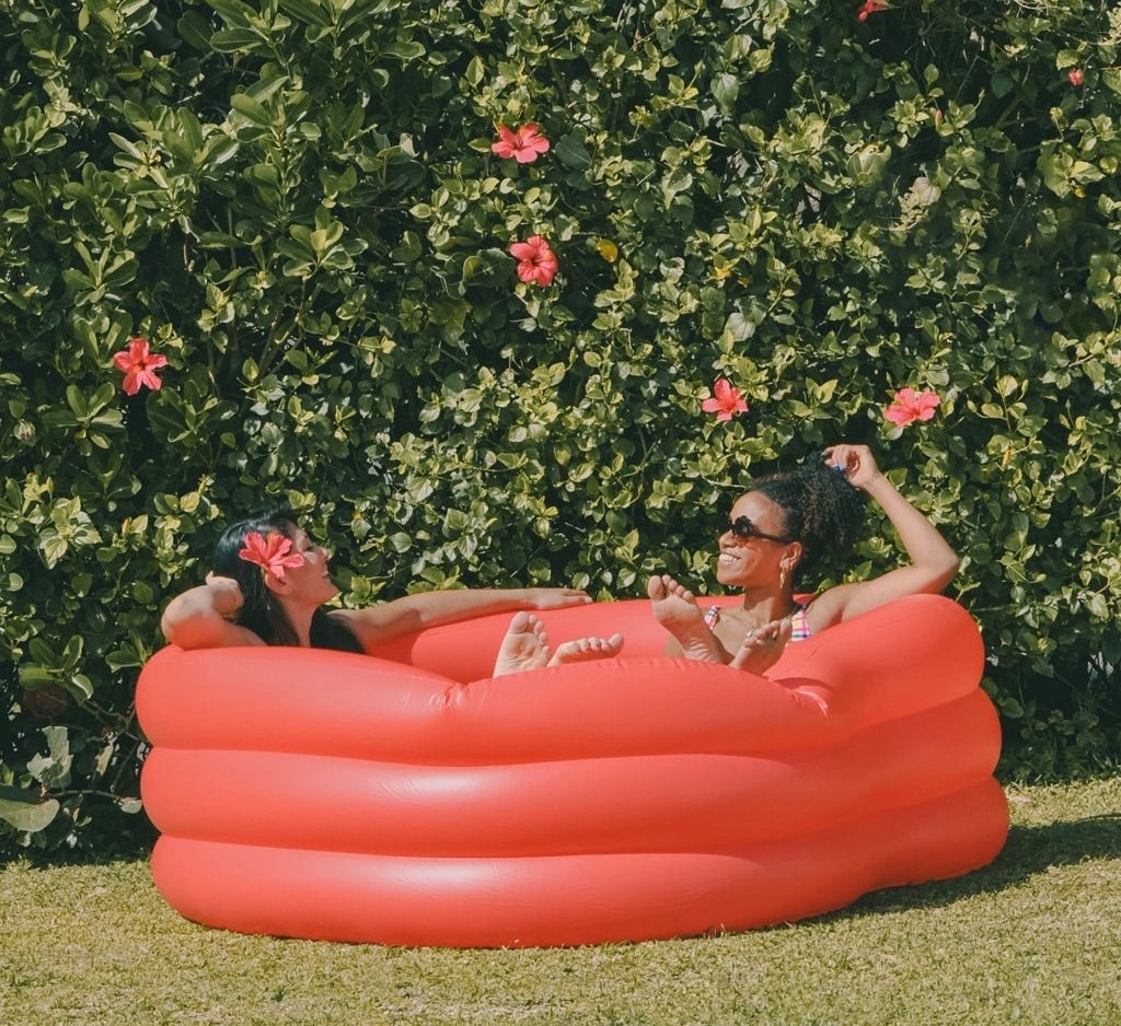 Two people lounging in a red heart-shaped inflatable pool