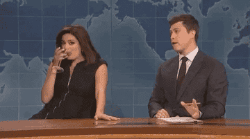 a gif of cecily strong spitting out a drink on colin jost