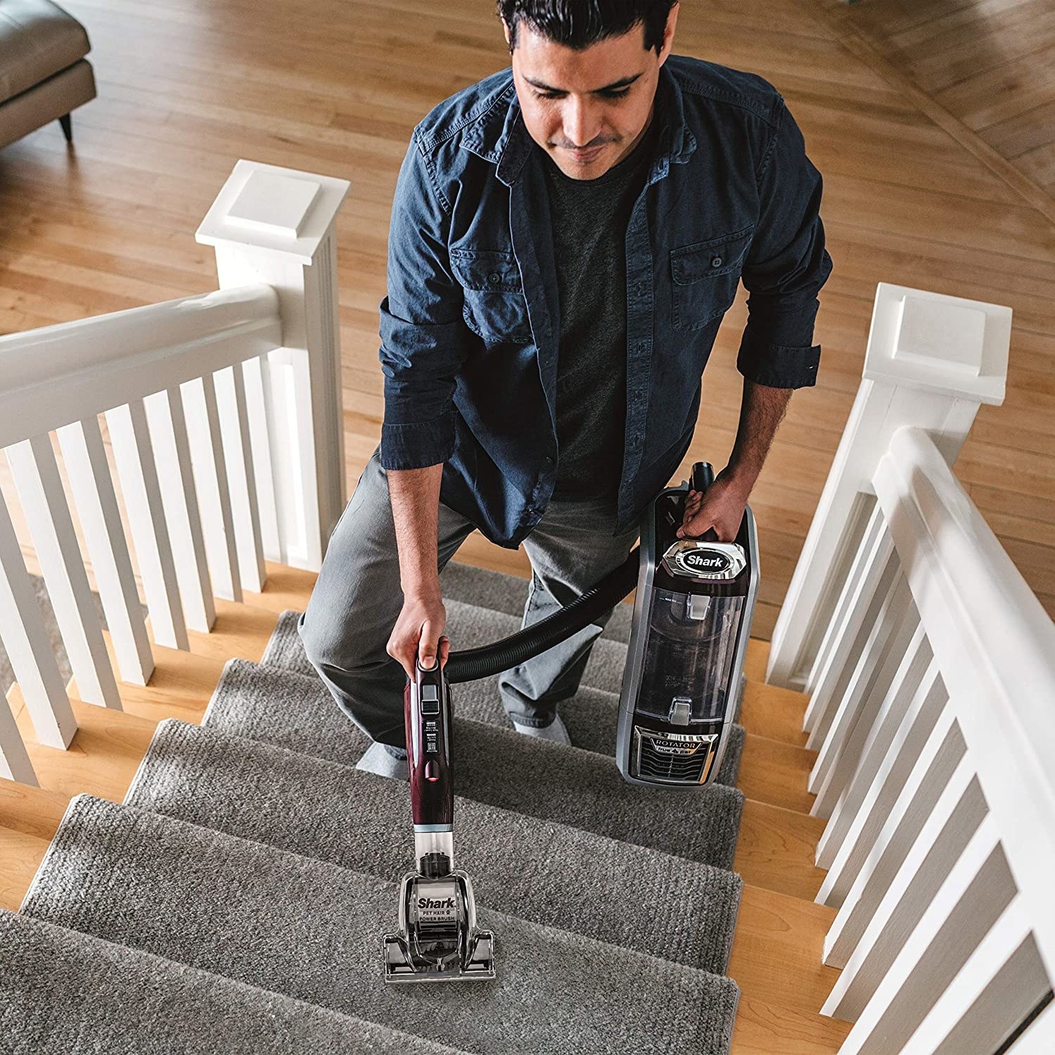 model vacuums stairs while holding the pod in one hand and the brush nozzle in the other