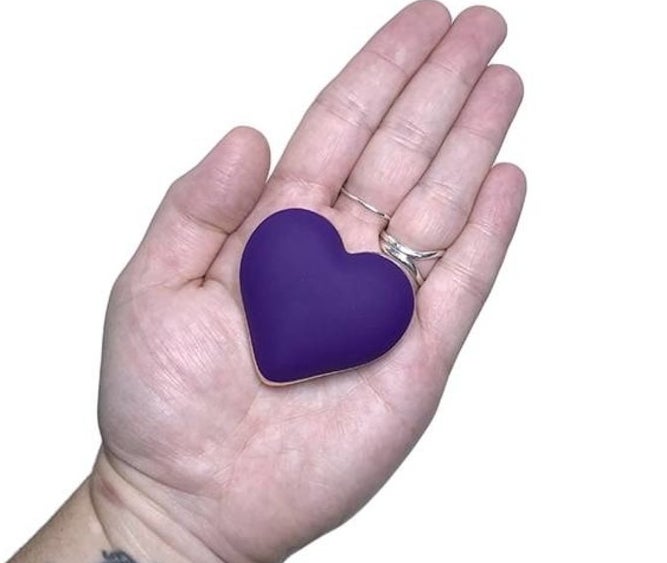 Model holding purple heart-shaped vibrator in palm