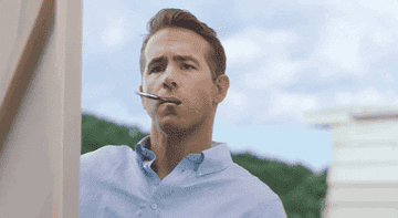 Ryan Reynolds moves away from a canvas with a paintbrush in his mouth