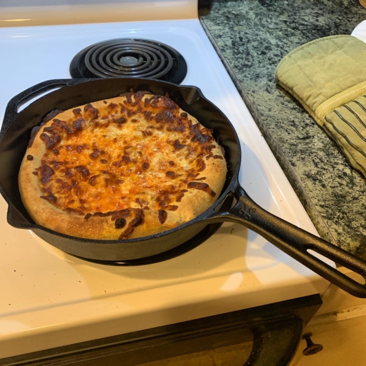 reviewer photo of the cast-iron pan being used to make cheesy bread on the stovetop