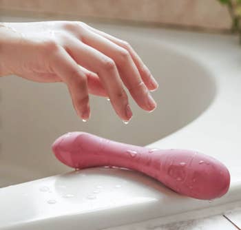 Model reaching for wet red vibrator on tub