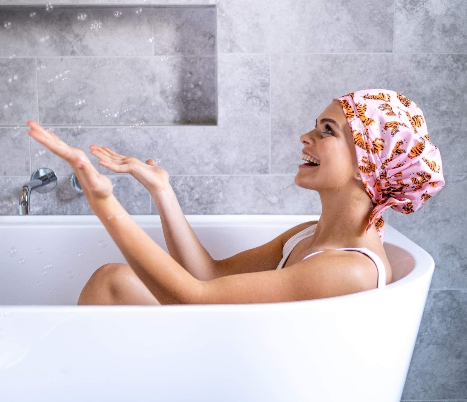A person sitting in a bath tub while wearing the adjustable shower cap
