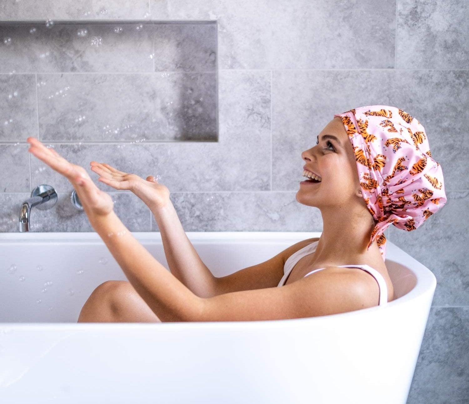 A person sitting in a bath tub while wearing the adjustable shower cap