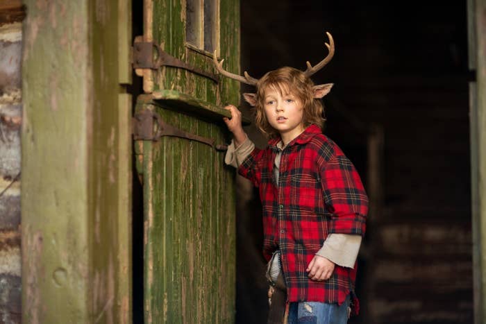 Actor Christian Convery, wearing deer antlers and a red flannel shirt, stands by an open door