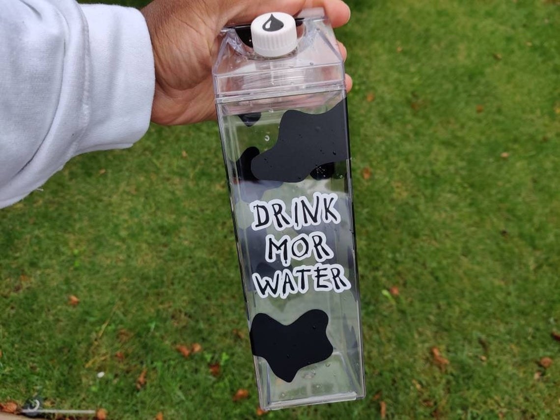hand holding clear acrylic water bottle with cow print and &quot;drink mor water&quot; in a similar font as chick-fil-a advertisements