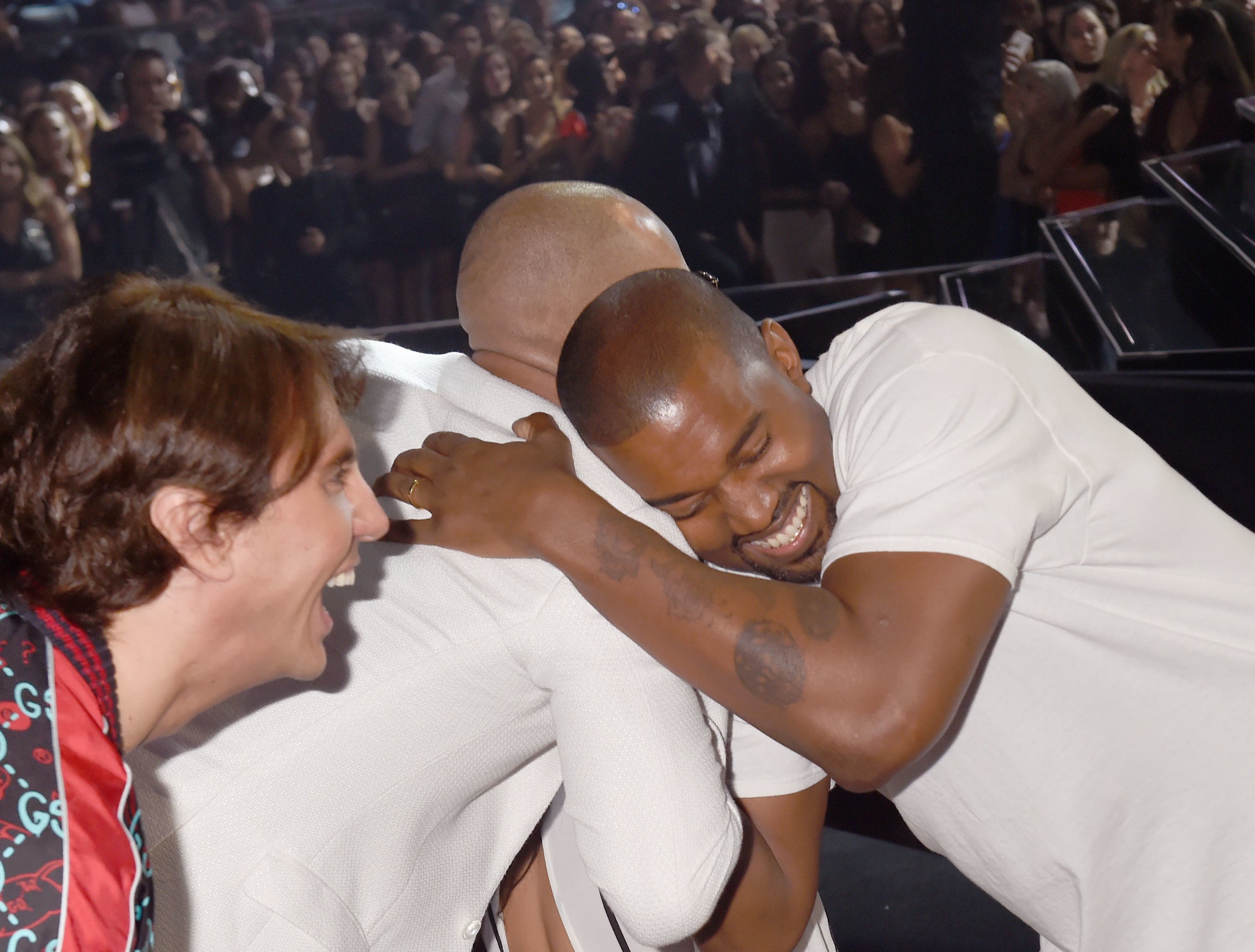 Jonathan leans over and smiles while Kanye hugs another friend