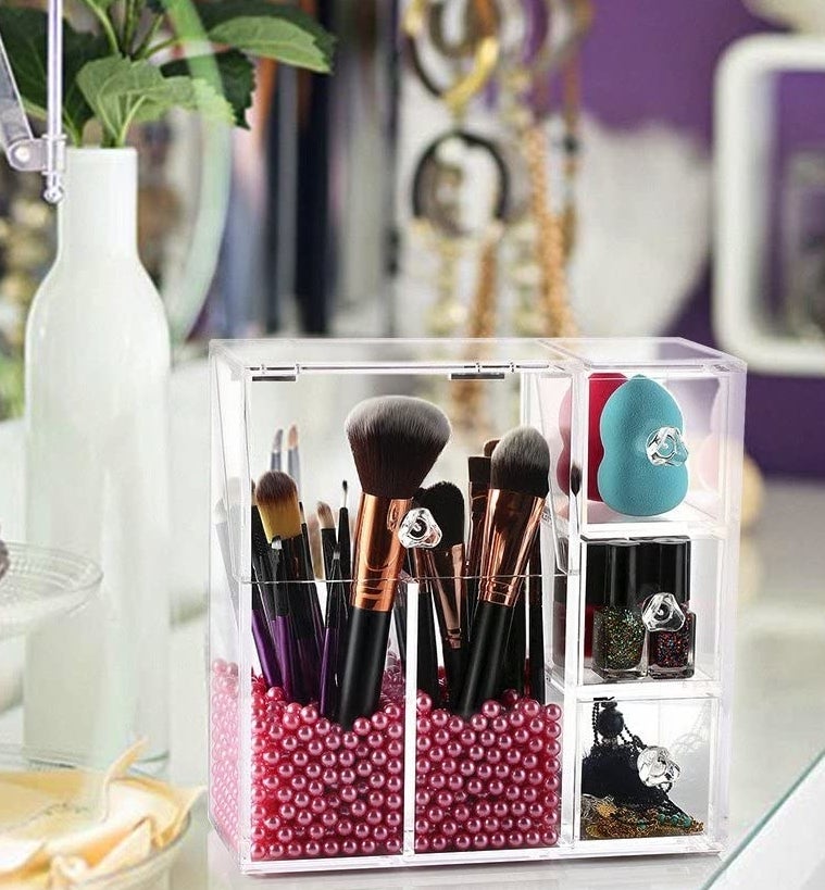 rectangular organizer with three vertically-stacked cube drawers on one side and two lidded tall cups for brushes filled about 1/4 with beads on the other