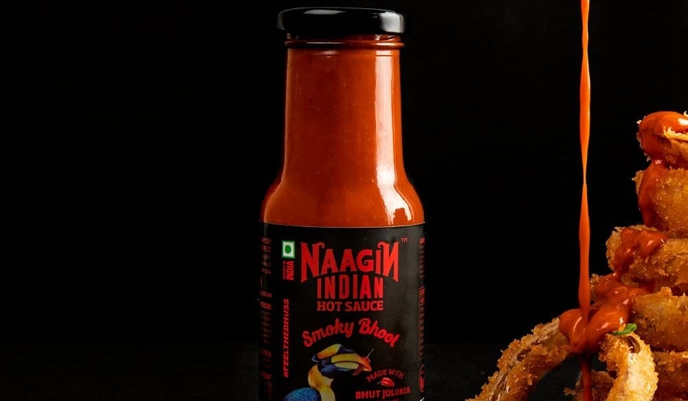 Naagin Smoky Bhoot hot sauce being poured on onion rings next to its bottle.