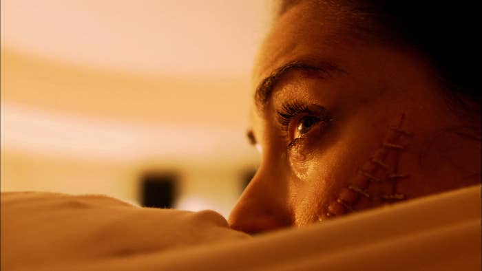 a girl with her mouth sewn to another person's anus, her eyes filled with fear
