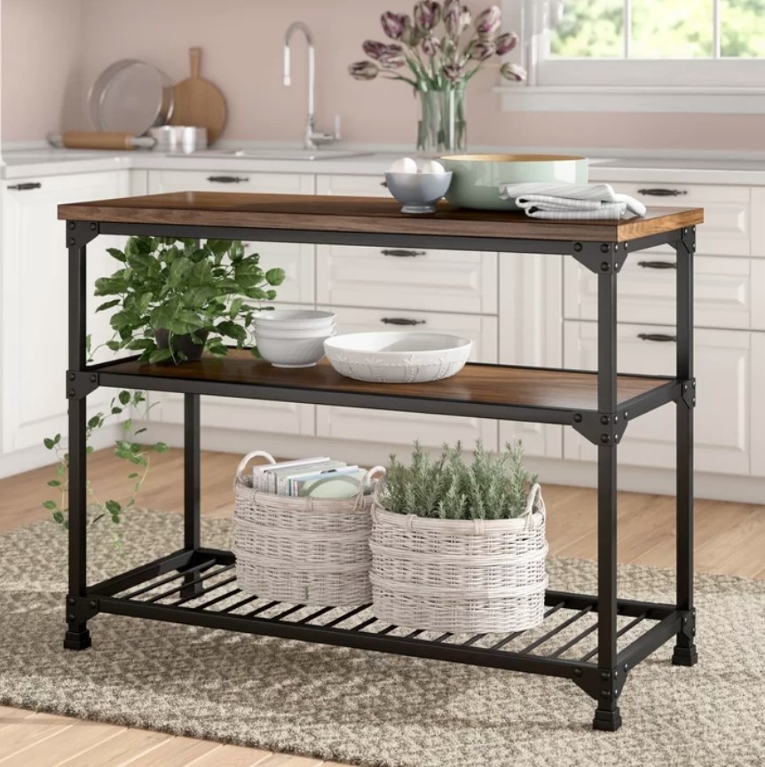 A steel and wood kitchen island with three shelves filled with plants and kitchen items