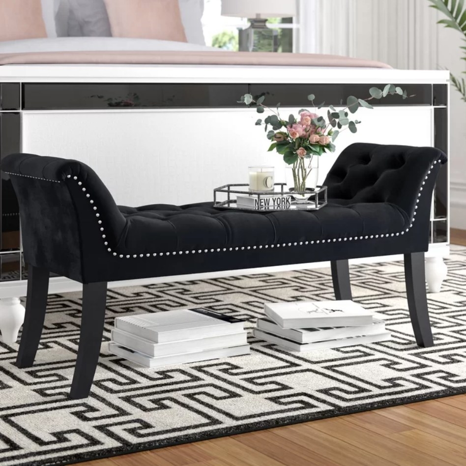 A black velvet upholstered bench with silver nail head details