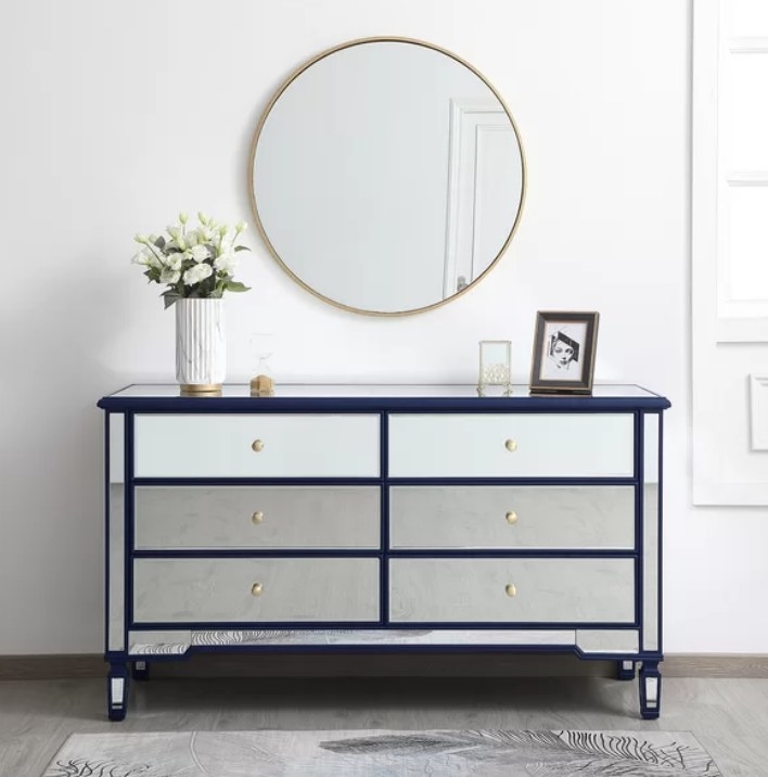 A six drawer double mirrored dresser with blue accenting with a frame and flowers atop