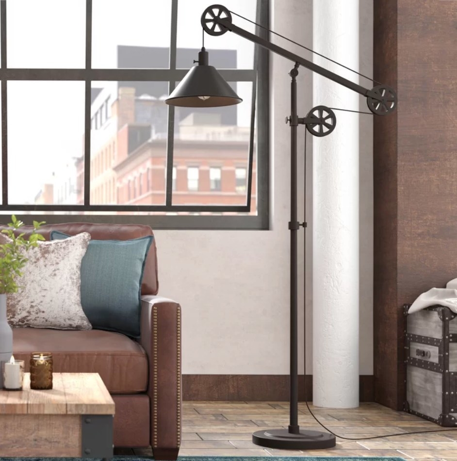 An industrial style, black floor lamp standing next to a couch in a living room