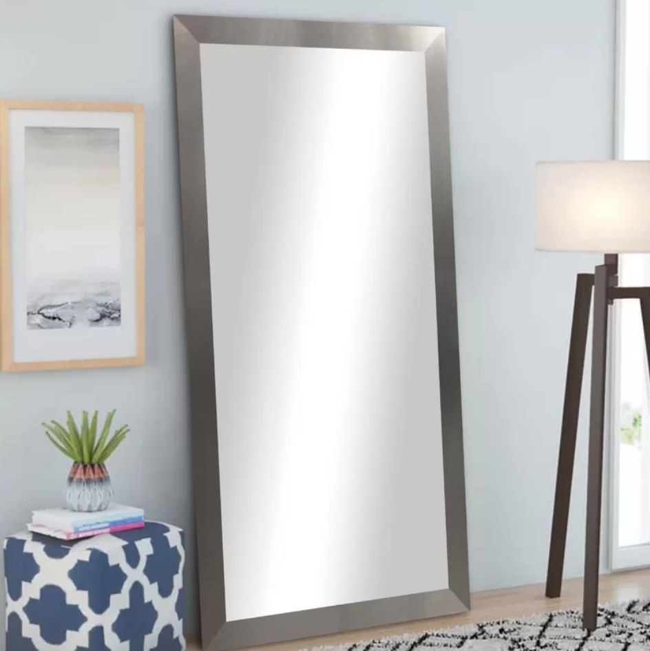 A silver wood framed floor length mirror leaning against a wall