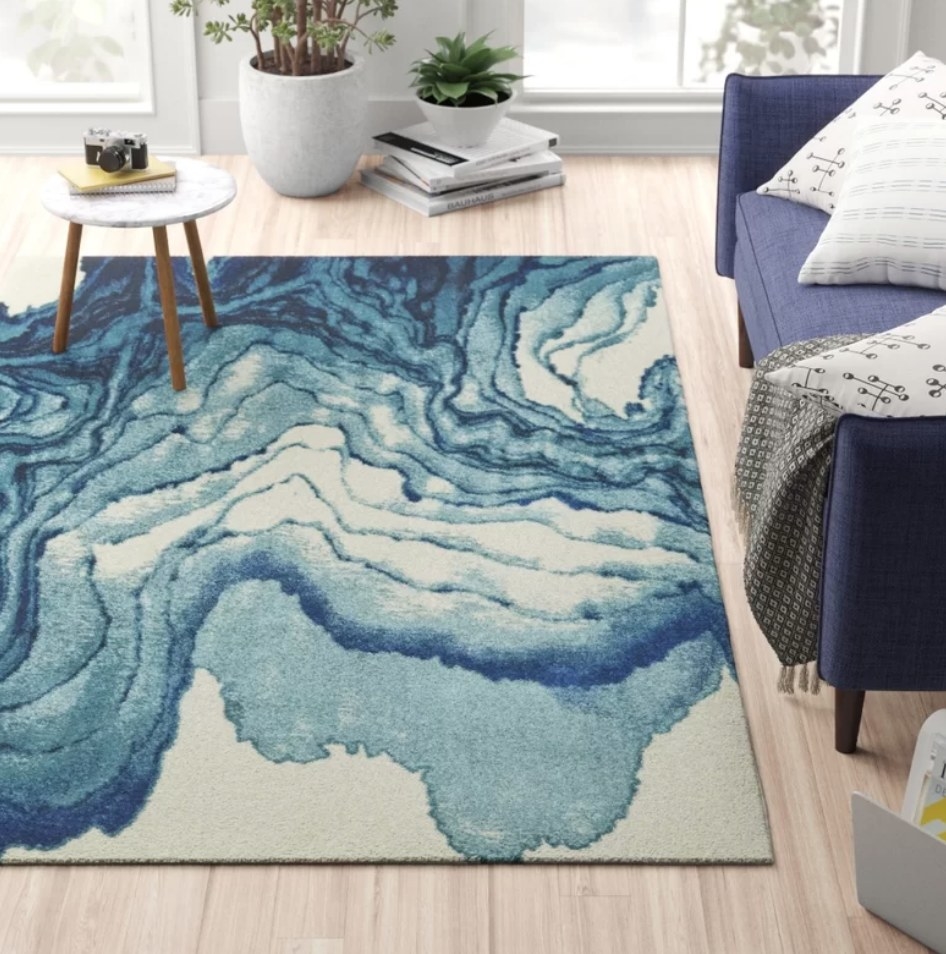 An abstract blue, rectangular area rug with a small coffee table atop in a living room