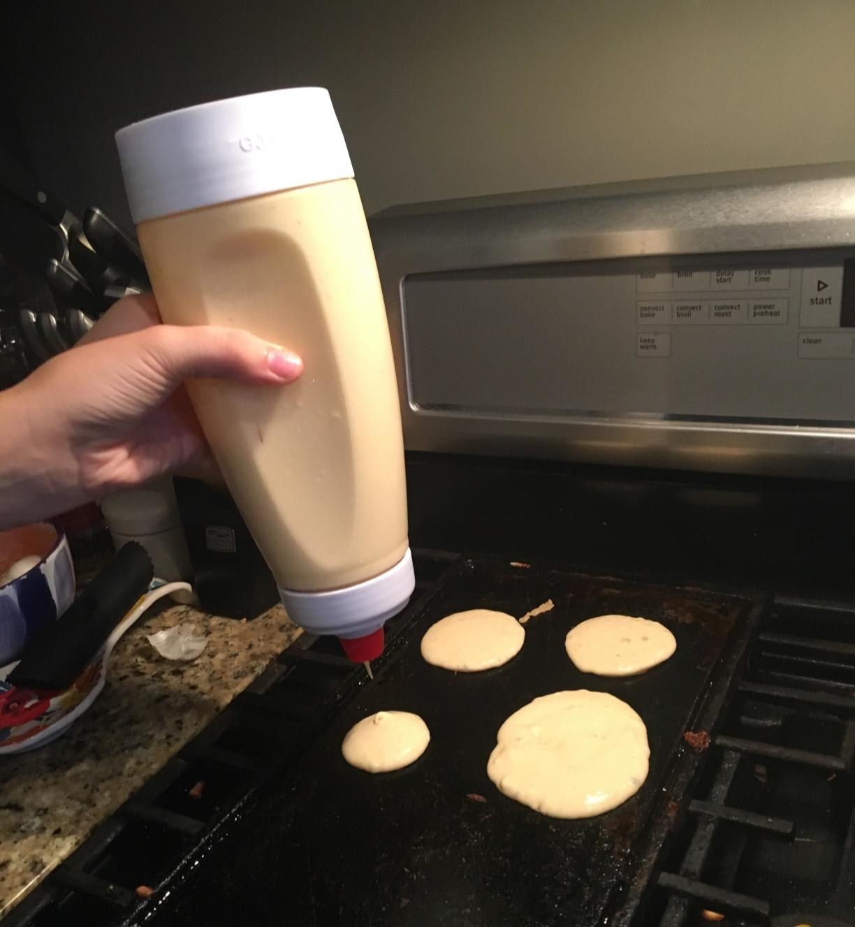 hand holding a bottle full of batter and pouring out pancake circles onto a griddle