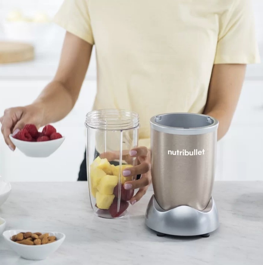 A 32oz, NutriBullet personal blender being filled with fruit my a model on a countertop