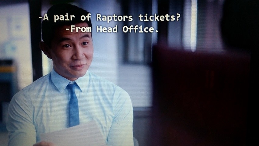 Jung wearing a dress shirt and tie is incredulous about receiving a pair of Raptors tickets