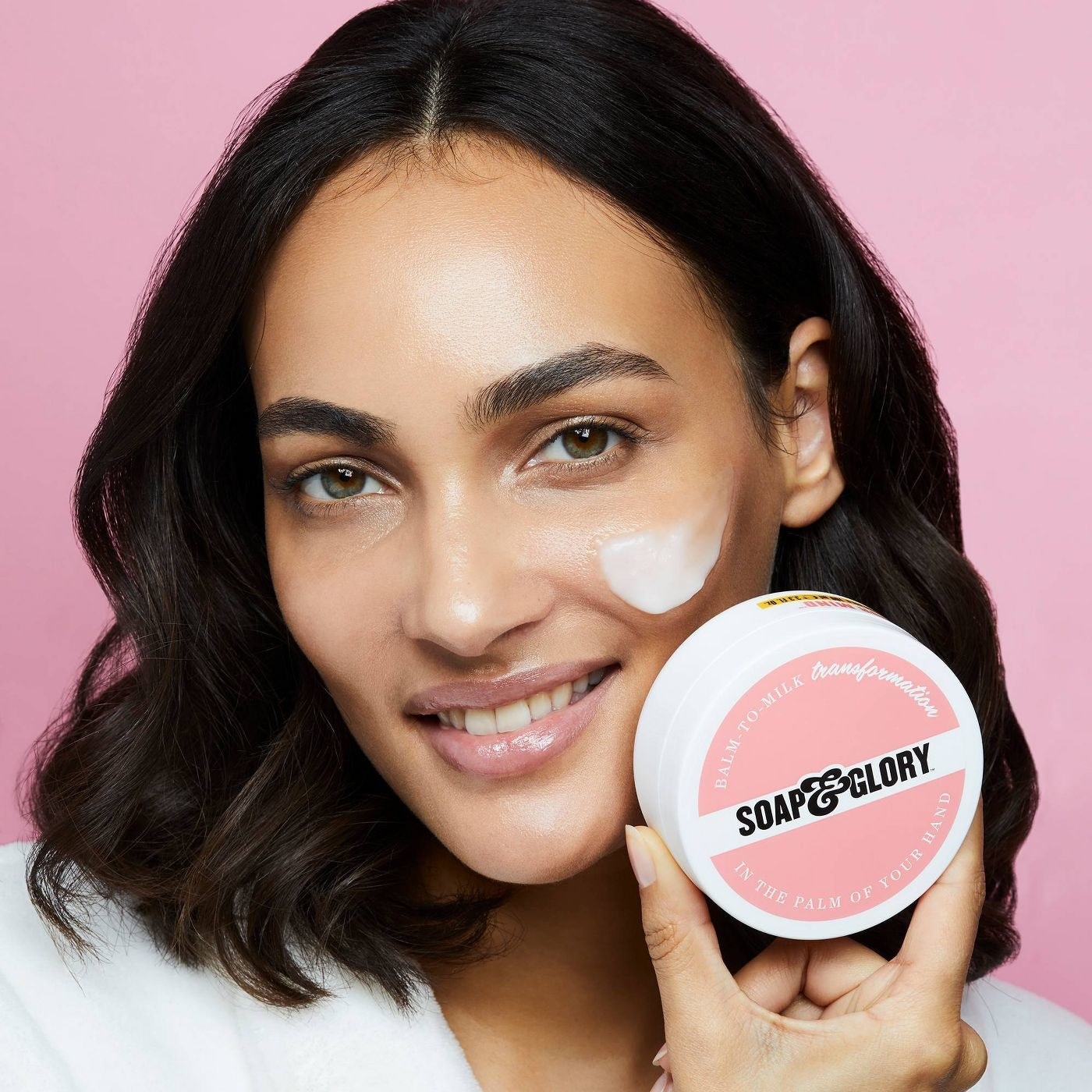 A model has a dollop on the balm on their face, and you can see the milky texture