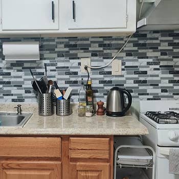 a reviewer photo of the kitchen with the peel and stick backsplash applied to the wall 