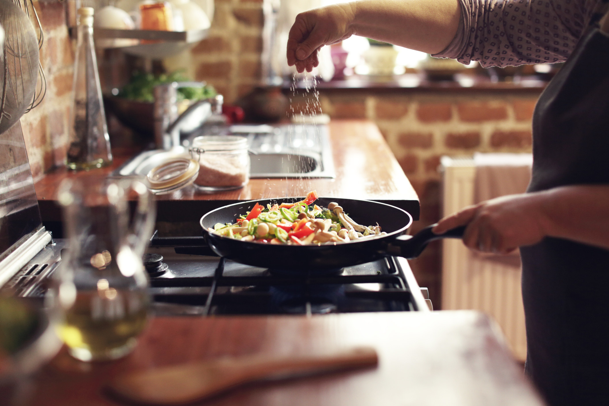 A woman salting her vegetables as they cook in the pan.