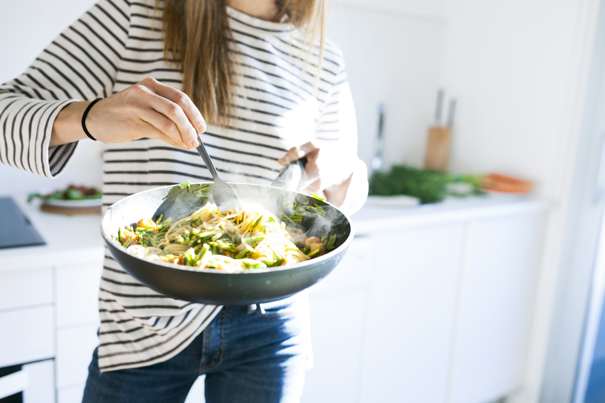 A woman twirling pasta in the pan.