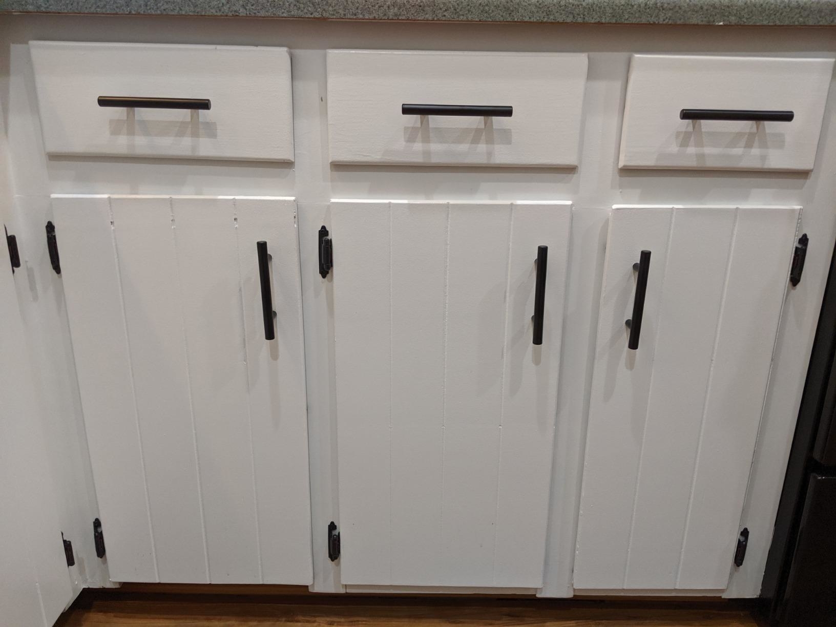 a review image of white cabinets and drawers with the black hardware installed