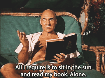 A bald man in an open shirt lounges with a book in hand, saying that all he requires is to sit in the sun and read his book, alone