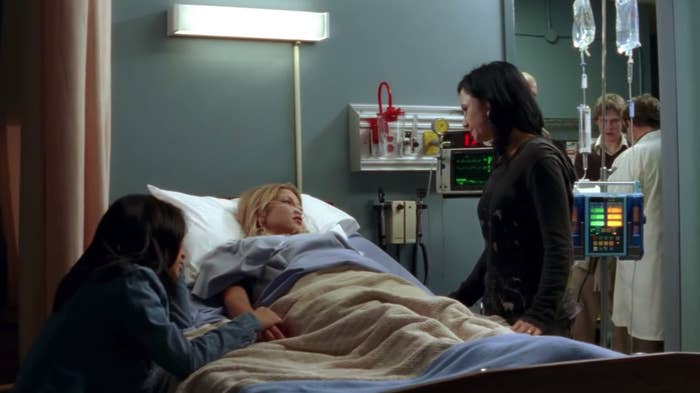 emma lying in a hospital bed surrounded by her mom and friend