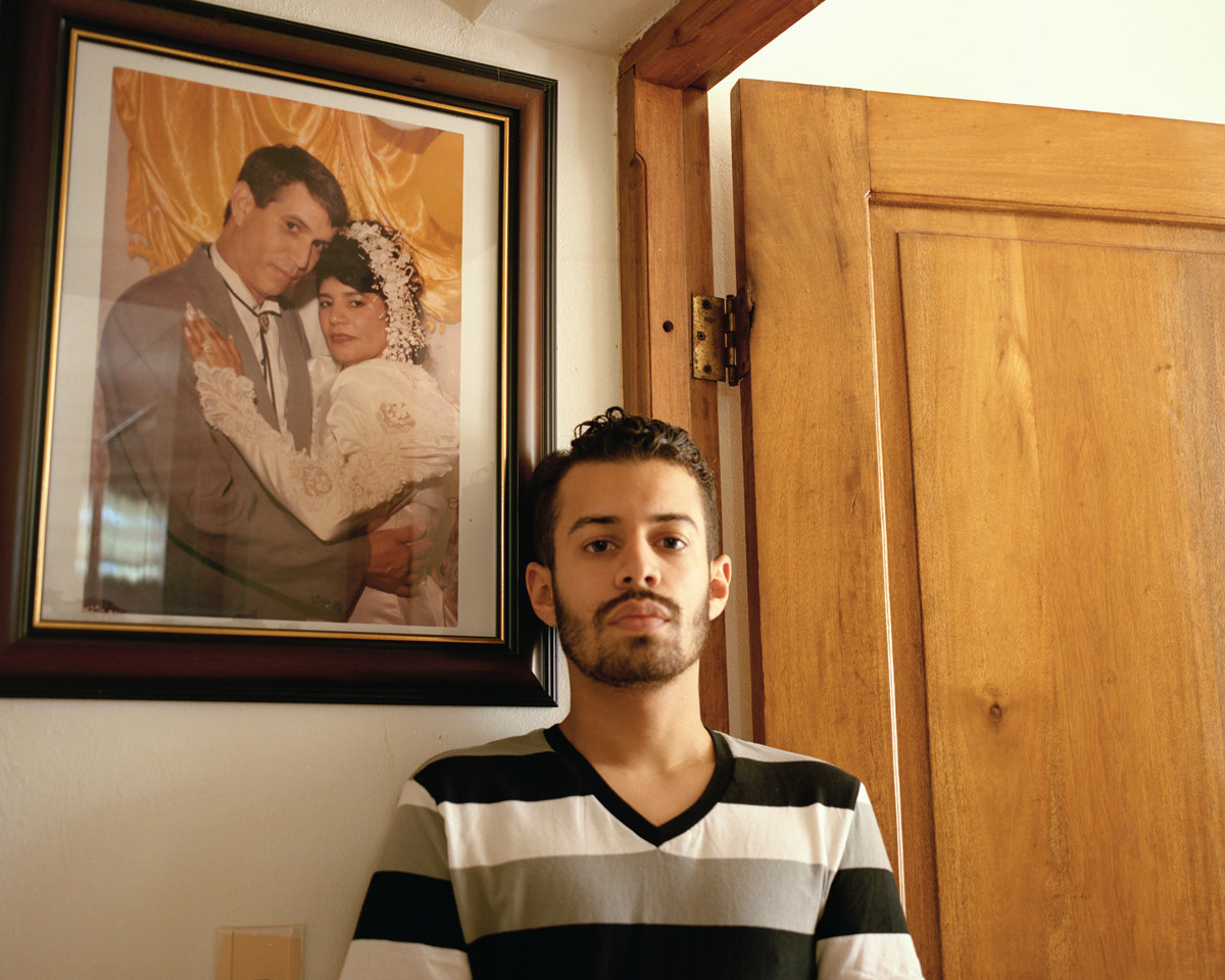 The photographer in a striped shirt, facing the camera under a photograph of his parents on their wedding day 