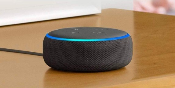 An Amazon Echo Dot in black on a desk.
