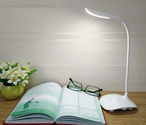 A desk lamp in white next to an open notebook and a flowerpot.