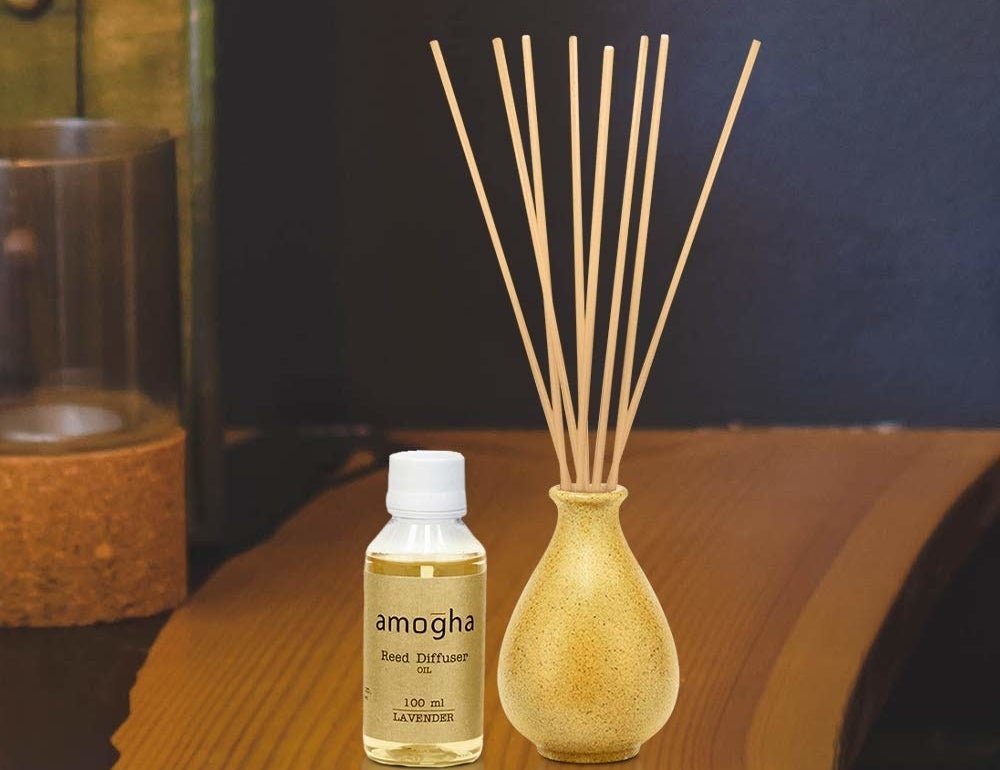 A brown reed diffuser on a desk next to a bottle of lavender reed diffuser oil.