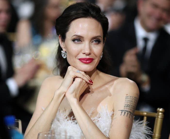 Angelina sits at a table with her arm tattoos visible