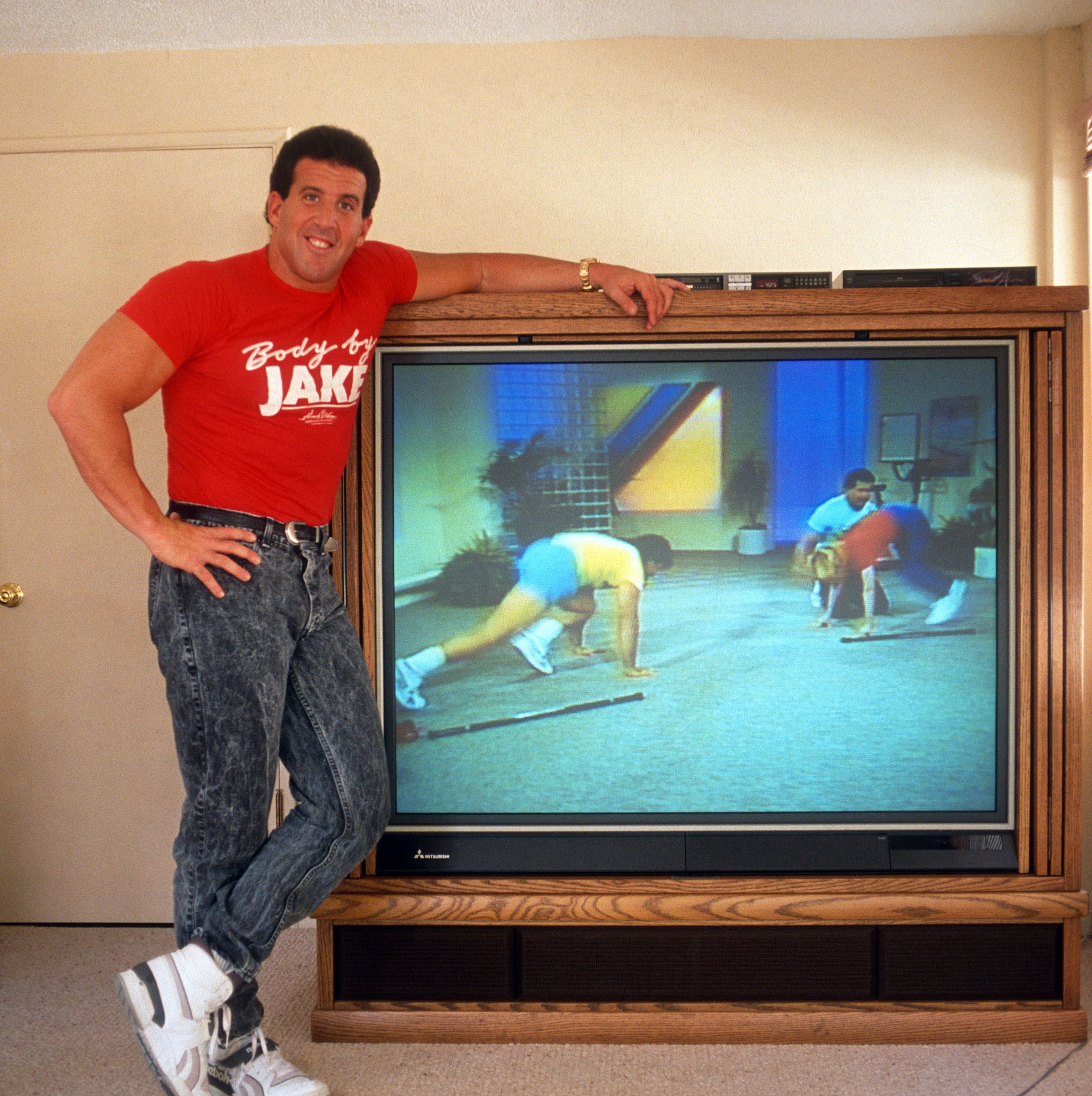 Body by Jake standing next to giant TV