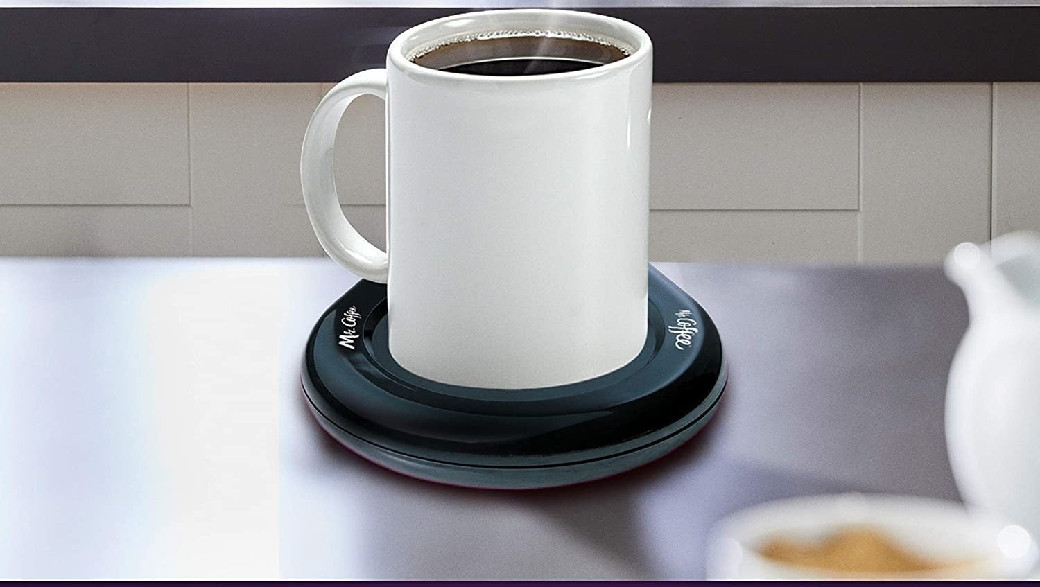 A black cup warmer on a counter with a hot cup of coffee on it.