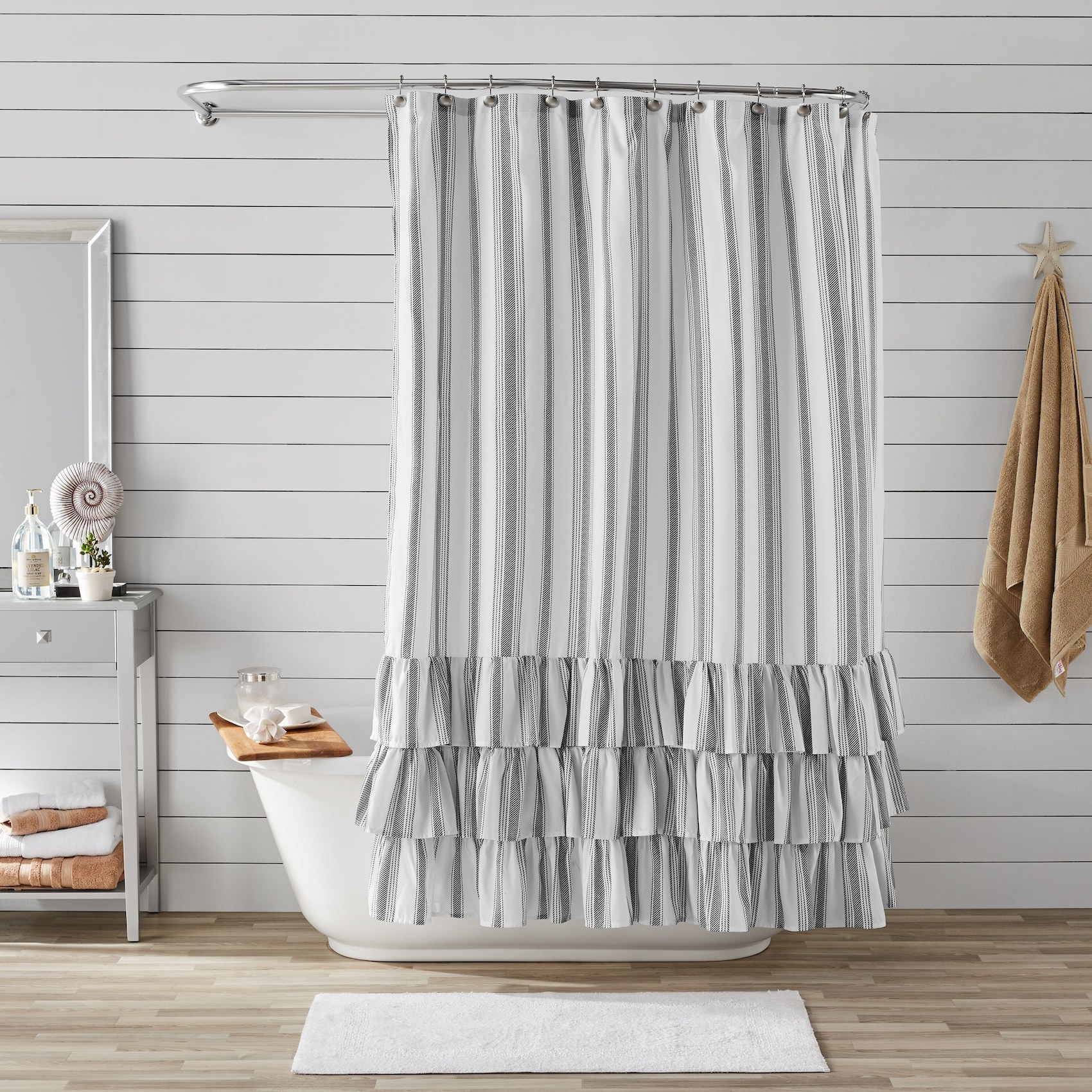 The shower curtain with vertical gray and white stripes and three tiers of ruffles on the bottom hanging in front of a shower in a bathroom