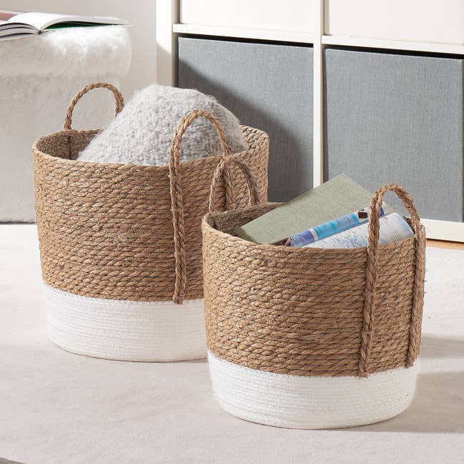 The two baskets with white bottoms and natural tops holding extra blankets and books
