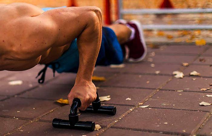 Model goes down in push-up position while holding black push-up handle bars on floor