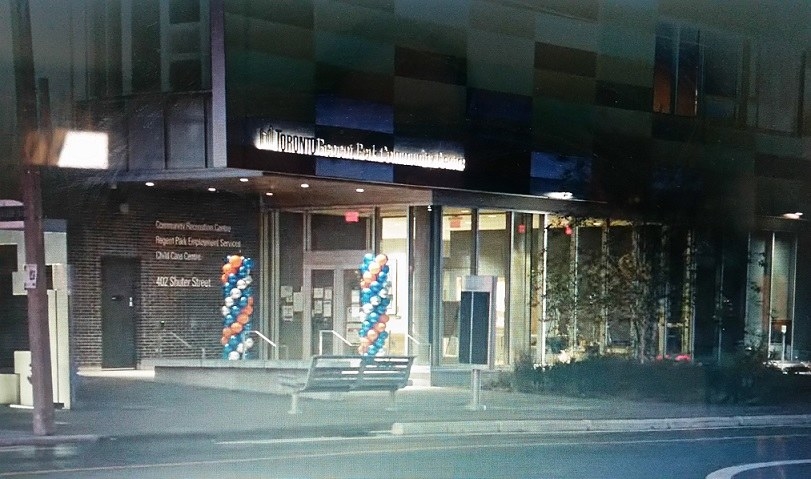 The Regent Park Community Centre is shown from the street with red, white, and blue balloons flanking the doorway
