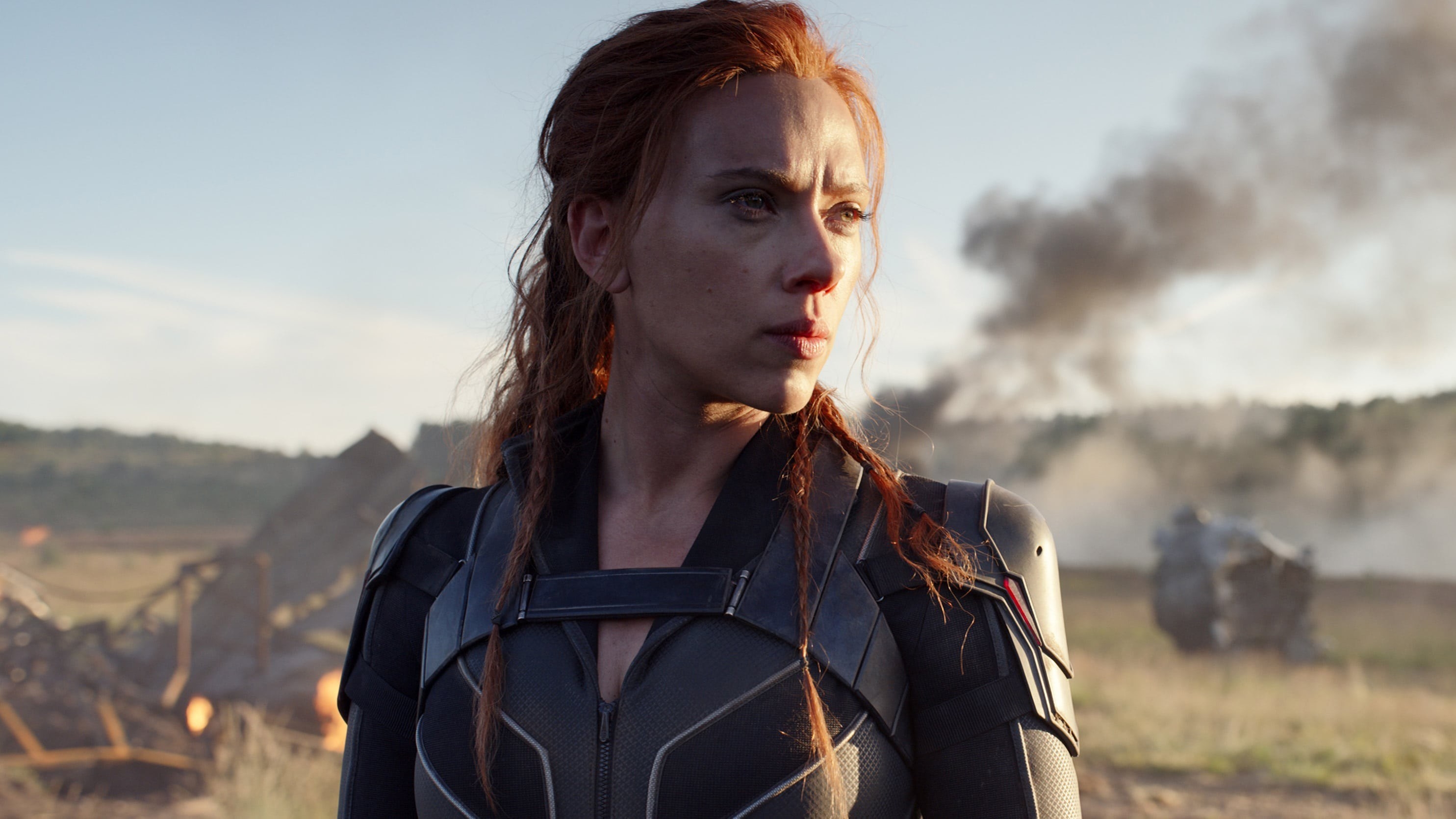 Black Widow looks into the distance in front of a fiery scene