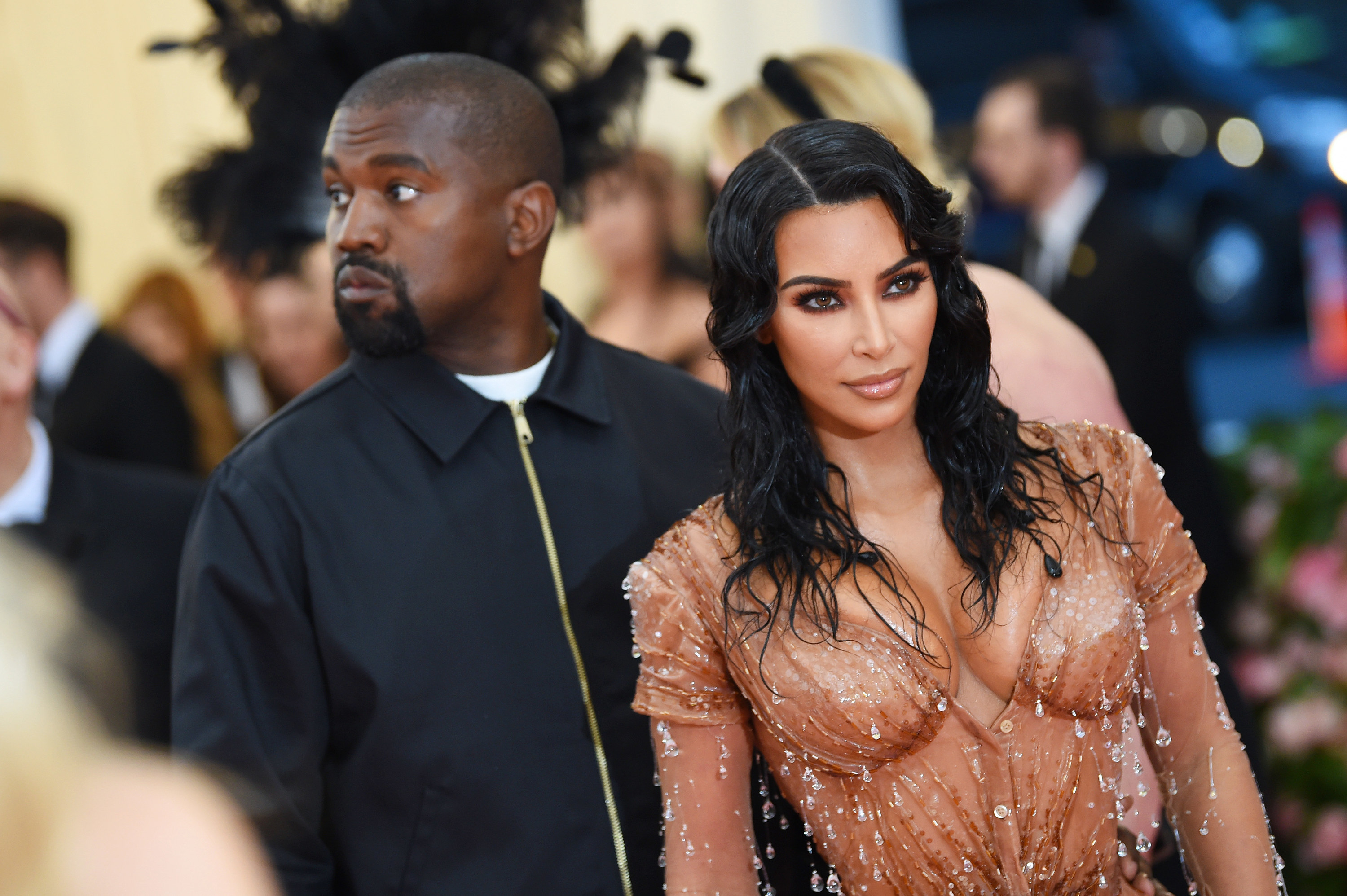 Kim in a corset dress stands in front of Kanye in a black pullover jacket