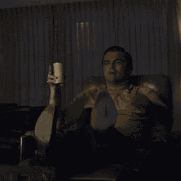 Leonardo DiCaprio sitting down and pointing while holding a cup