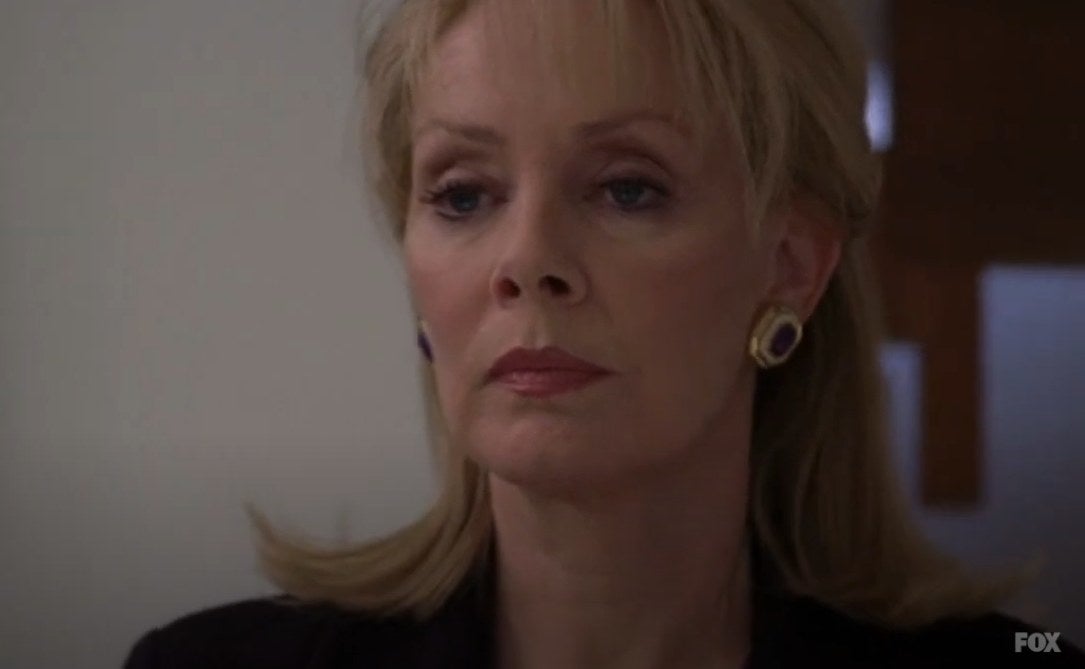 A woman (Jean Smart) in a formal outfit looking at something offscreen