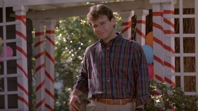 rick moranis in plaid shirt and khakis smiles slightly