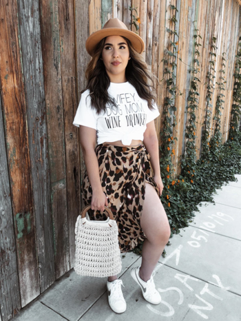 reviewer photo of wearing the wrap leopard print skirt with white sneakers, a graphic T-shirt, and hat