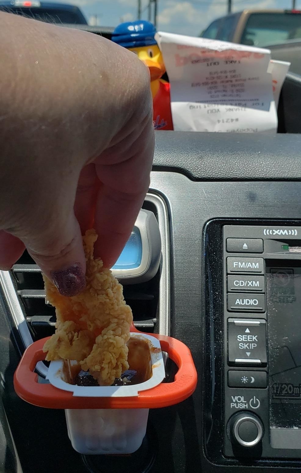 reviewer dunking a chicken tender in a sauce packet that is attached to a sauce holder